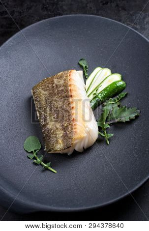 Fried Danish skrei cod fish filet with baby zucchini and lettuce as top view on a modern design plate 