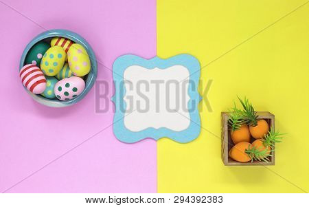 Easter Eggs And Carrots On A Pink And Yellow Background, With A Blue Frame In The Centre With Copy S