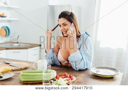 Sexy Girl In Bra And Short Sitting At Table And Talking On Smartphone