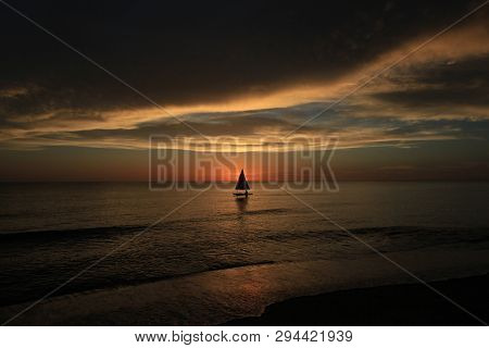 Captiva Island, Florida 08-05-2015 Small Sailboat In Partial Silhouette Against The Setting Sun In T