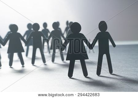 Black paper figure of a couple in front of a crowd of paper people holding hands on white surface. Social movement, protest, leadership concept.