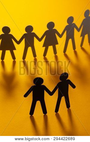Black paper figure of male couple in front of a crowd of paper people holding hands on orange surface. Social movement, protest, minorities concept.
