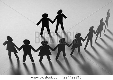 Black paper figure of male couple in front of a crowd of paper people holding hands on white surface. Social movement, protest, minorities concept.