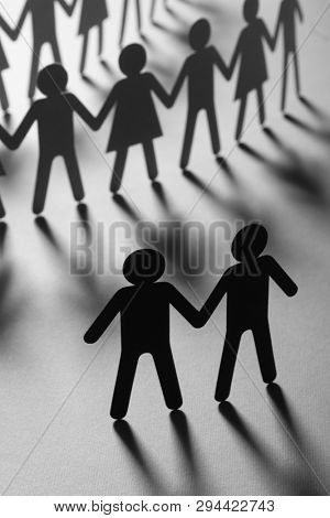Black paper figure of male couple in front of a crowd of paper people holding hands on white surface. Social movement, protest, minorities concept.