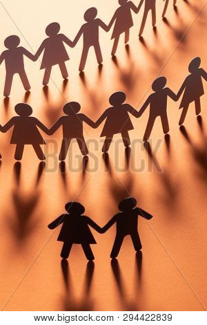 Black paper figure of a couple in front of a crowd of paper people holding hands on red surface. Social movement, protest, leadership concept.