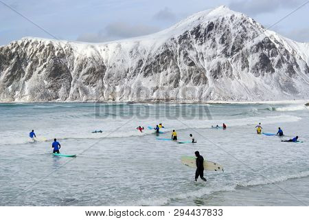 FLAKSTAD BEACH, LOFOTEN ARCHIPELAGO, 26 MARCH, 2019: Young men surfing in arctic conditions at Flakstag Beach, Lofoten, Norway, Europe