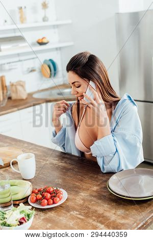 Sexy Girl In Bra And Short Sitting At Table And Talking On Smartphone