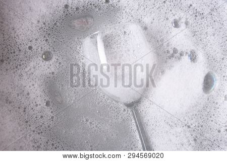 Overhead shot of a dishpan with a single wine glass immersed in soapy water.