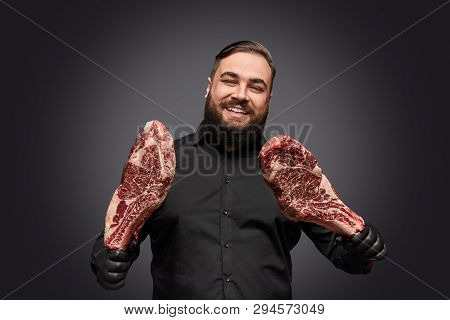 Attractive Bearded Meatman In Latex Gloves Cheerfully Smiling And Holding Two Pieces Of High Quality