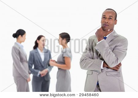 Close-up of a businessman looking up with a hand on his chin and three co-workers talking seriously in the background