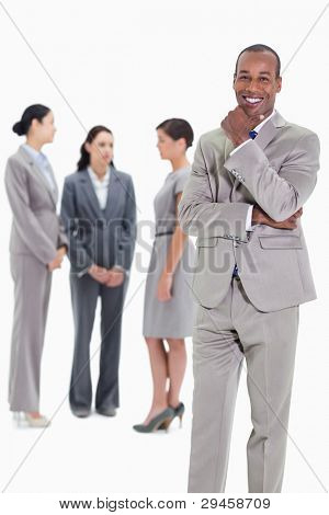 Happy businessman with a hand on his chin and three co-workers talking seriously in the background