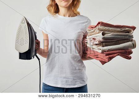 Partial Woman In T-shirt Holding Iron And Folded Ironed Clothes Isolated On Grey