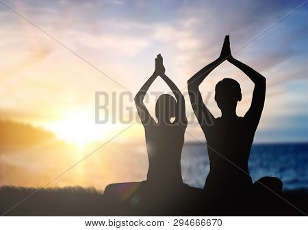 mindfulness, spirituality and outdoor yoga - silhouettes of couple meditating in lotus pose over sunset and sea background