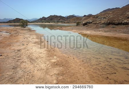 Arabian peninsula landscape with cracked mud, puddle and dry mountains in Fujairah, United Arab Emirates
