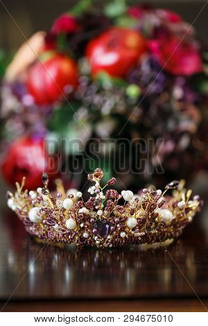 Wedding Crown With Multi-colored Crystals And White Pearls Lies On A Glossy Table Against The Backgr