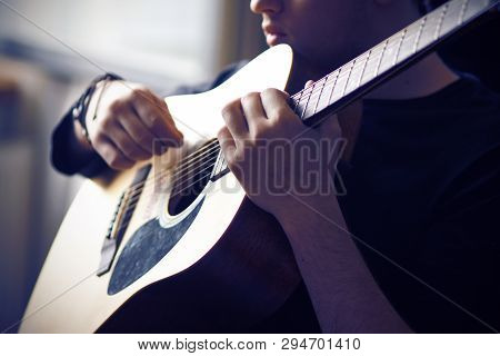 A Professional Musician In Black Clothes Plays His Favorite Acoustic Six-string Guitar, Holding The 
