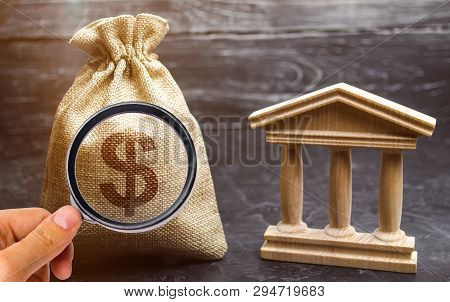 A Bag With Dollar Money And A Bank Or Government Building. Deposits, Investment In The Budget. Grant