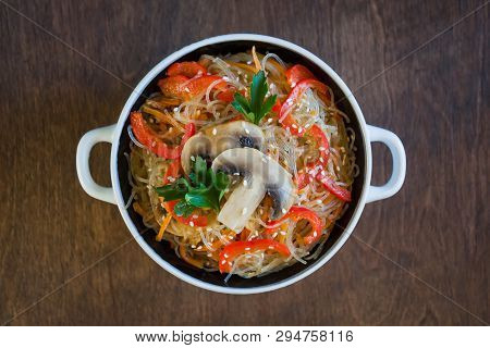 Glass Noodles With Vegetables And Mushrooms In A Plate On A Brown Background. Top View, Close-up