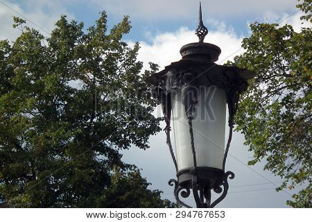 Classic Vintage Street Lamp On A Background Of Green Trees And Blue Sky.