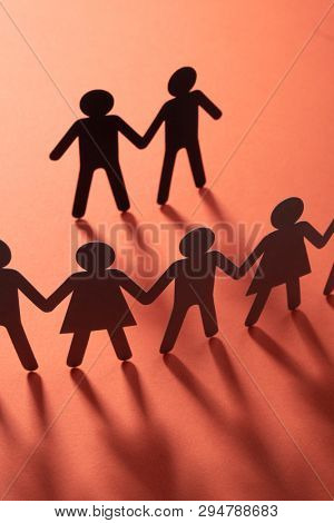 Black paper figure of male couple in front of a crowd of paper people holding hands on redsurface. Social movement, protest, minorities concept.