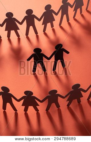 Black paper figure of male couple in front of a crowd of paper people holding hands on redsurface. Social movement, protest, minorities concept.