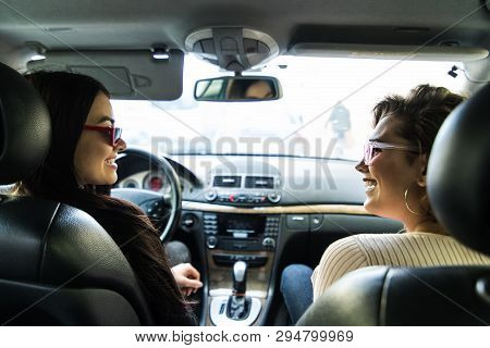 Smiling Happy Young Woman Giving Her Friend A Lift In Her Car In Town, Through The Open Side Window 