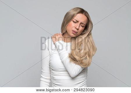 Closeup Studio Portrait Of Cute Unhealthy Young Blonde Female In White Top With Pain In Her Neck And