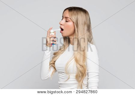 Studio Portrait Of Attractive Upset Young Blonde Woman Using A Spray To Treat Sore Throat/throat Pai