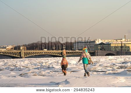 Mom And Child In Bright Clothes Walking On The Ice Of Frozen Neva In Sunny Winter Day, Trinity Bridg
