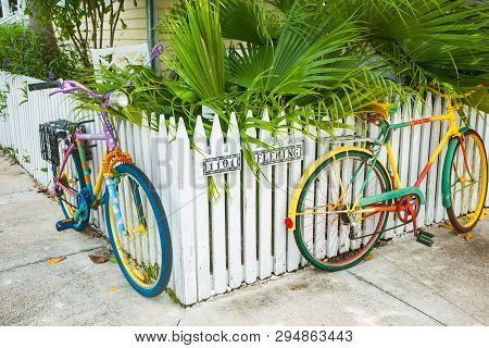 Key West Usa - June 26 2012;two Multi-colored Cycles Attached To White Picket Fence As Street Art On