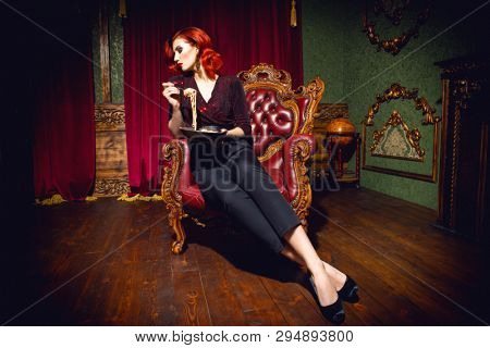 A full length portrait of a beautiful woman posing in the vintage interior and having a meal. Beauty, fashion, interior.