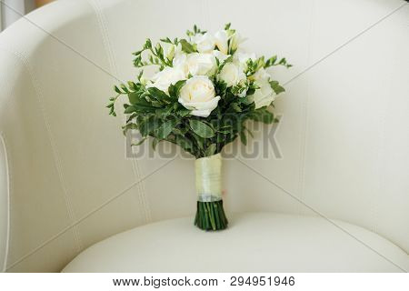A Wedding Bouquet Of White Roses And Freesias Is On The Bright Chair