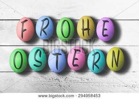 Frohe Ostern, German For Happy Easter, Written On Colored Easter Eggs Against White Wooden Table
