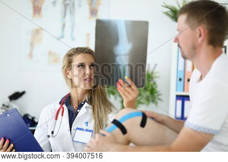 Doctor And Patient Look At X-ray Image Of Patient On Leg With Kinesiotape. Kinesio Tape Trauma Care 