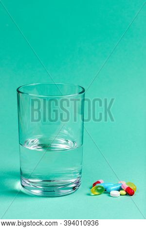 Colored Pharmaceutical Pills, Vitamins And A Glass Of Water.