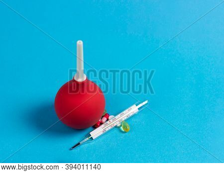 Enema, Mercury Thermometer And Medical Pills On A Blue Background.