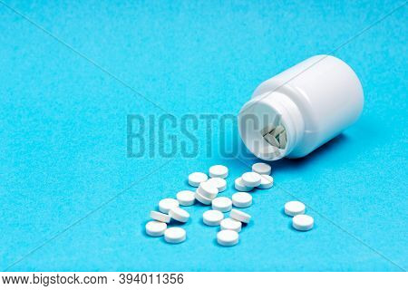 White, Overturned Medical Jar With Scattered Pills On A Blue Background. Medications.