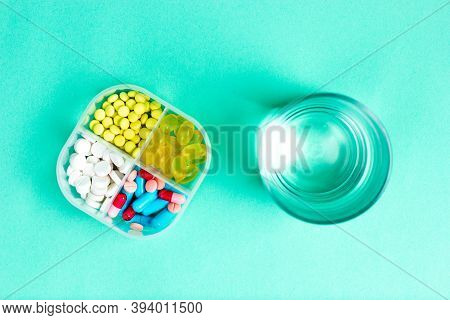 Medical Pills In A Pill Box And A Glass Of Water. View From Above.