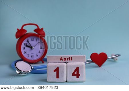 April 14st. White Wooden Calendar Blocks With Date, Clock And Stethoscope On A Blue Pastel Backgroun