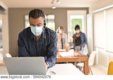 Man with surgical face mask and headest working on laptop in open space office