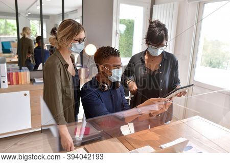 Coworkers in open space office, protected with plexiglas during 19-ncov pandemic
