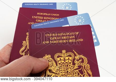 Hand holding United Kingdom British passports and EHIC European Union Health Insurance Cards. 