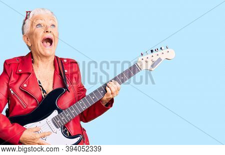 Senior beautiful woman with blue eyes and grey hair wearing a modern look playing electric guitar angry and mad screaming frustrated and furious, shouting with anger. rage and aggressive concept. 