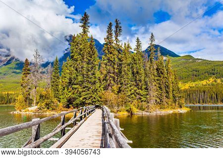  Rocky Mountains of Canada. Pyramid Lake. Narrow wooden bridge connects a small wooded islet with the lake shore. Active eco and photo tourism concept