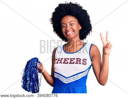 Young african american woman wearing cheerleader uniform holding pompom smiling looking to the camera showing fingers doing victory sign. number two. 