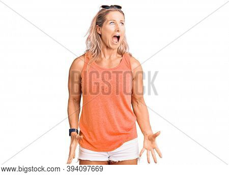 Middle age fit blonde woman wearing casual summer clothes and sunglasses angry and mad screaming frustrated and furious, shouting with anger. rage and aggressive concept. 