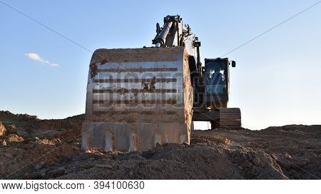 Excavator Working On Earthmoving At Open Pit Mining. Backhoe Digs Sand And Gravel On Blue Sky Backgr