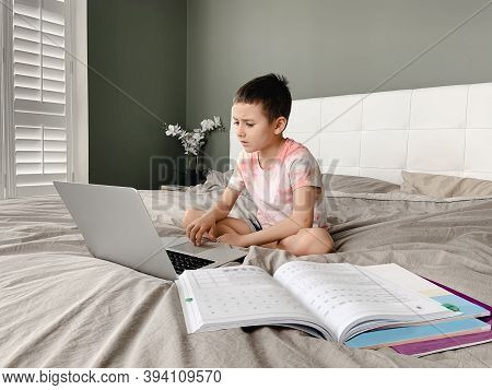 Caucasian Boy Child Sitting In Bed And Learning Online On Laptop Internet. Virtual Class Lesson On V