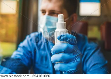 Young Caucasian Guy In A Protective Mask Holds An Antiseptic In His Hand With A Medical Glove