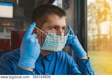 Young Caucasian Guy In Protective Gloves Puts On A Medical Mask In A Modern Electric Train And Looks